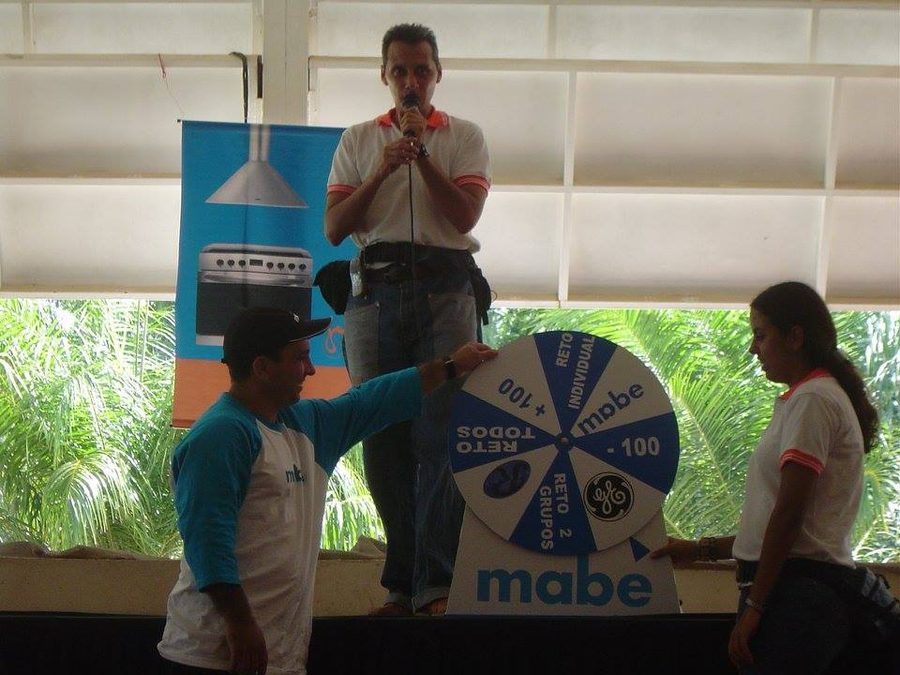 Animador con micrófono conduciendo una dinámica de retos junto a una ruleta con la marca Mabe y el logo de General Electric