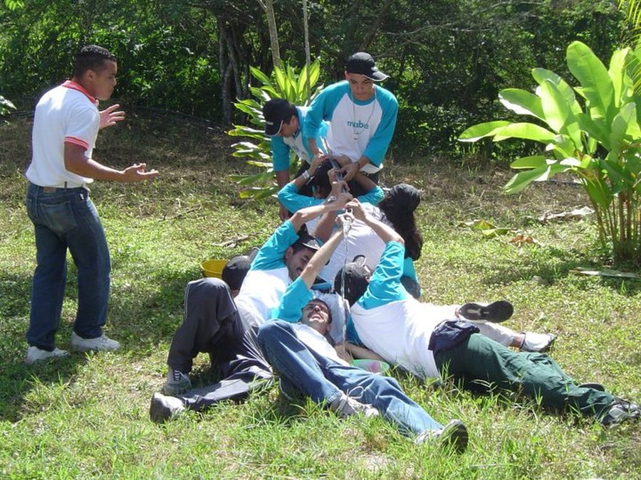 Equipo corporativo con camisetas de Mabe realizando un ejercicio de confianza sobre el césped, guiados por un facilitador