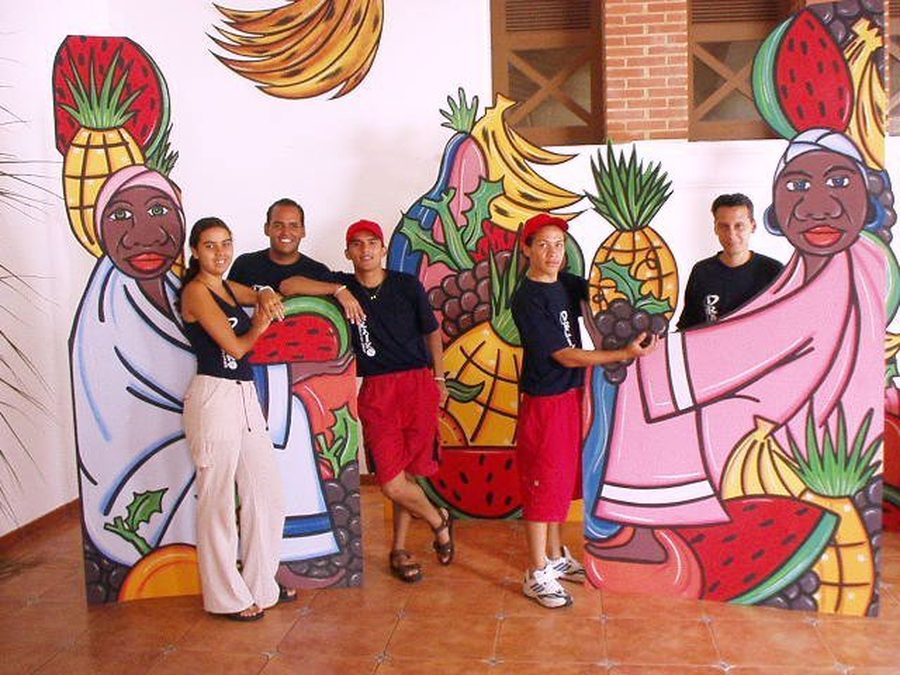 Equipo de animadores posando junto a paneles de escenografía pintados a mano con motivos de frutas y personajes tradicionales